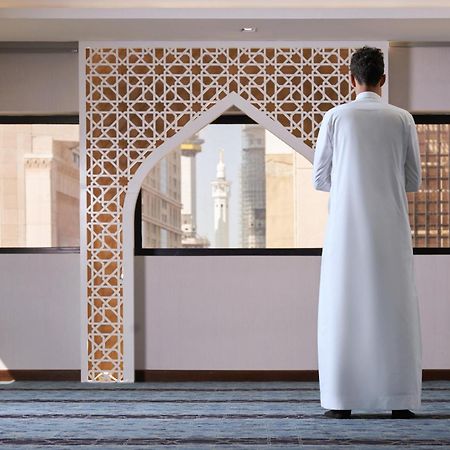 Makarem Ajyad Makkah Hotel Μέκκα Εξωτερικό φωτογραφία The photo depicts a person standing with their back facing the viewer, wearing a traditional white garment. They are in a spacious interior setting that features an ornate archway with intricate patterns, typical of Islamic architecture. Through the 