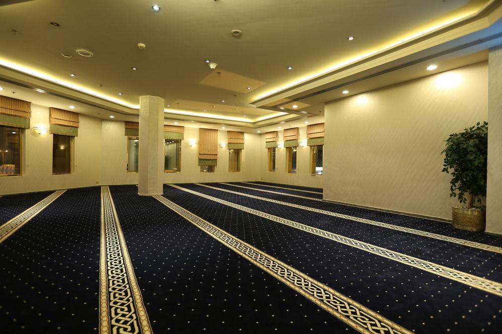 Makarem Ajyad Makkah Hotel Μέκκα Εξωτερικό φωτογραφία The photo shows a spacious indoor area with a plush blue carpet featuring a decorative pattern. The room is well-lit, with soft lighting along the ceiling. There are several windows, allowing natural light to enter, and a few plants are positioned ar