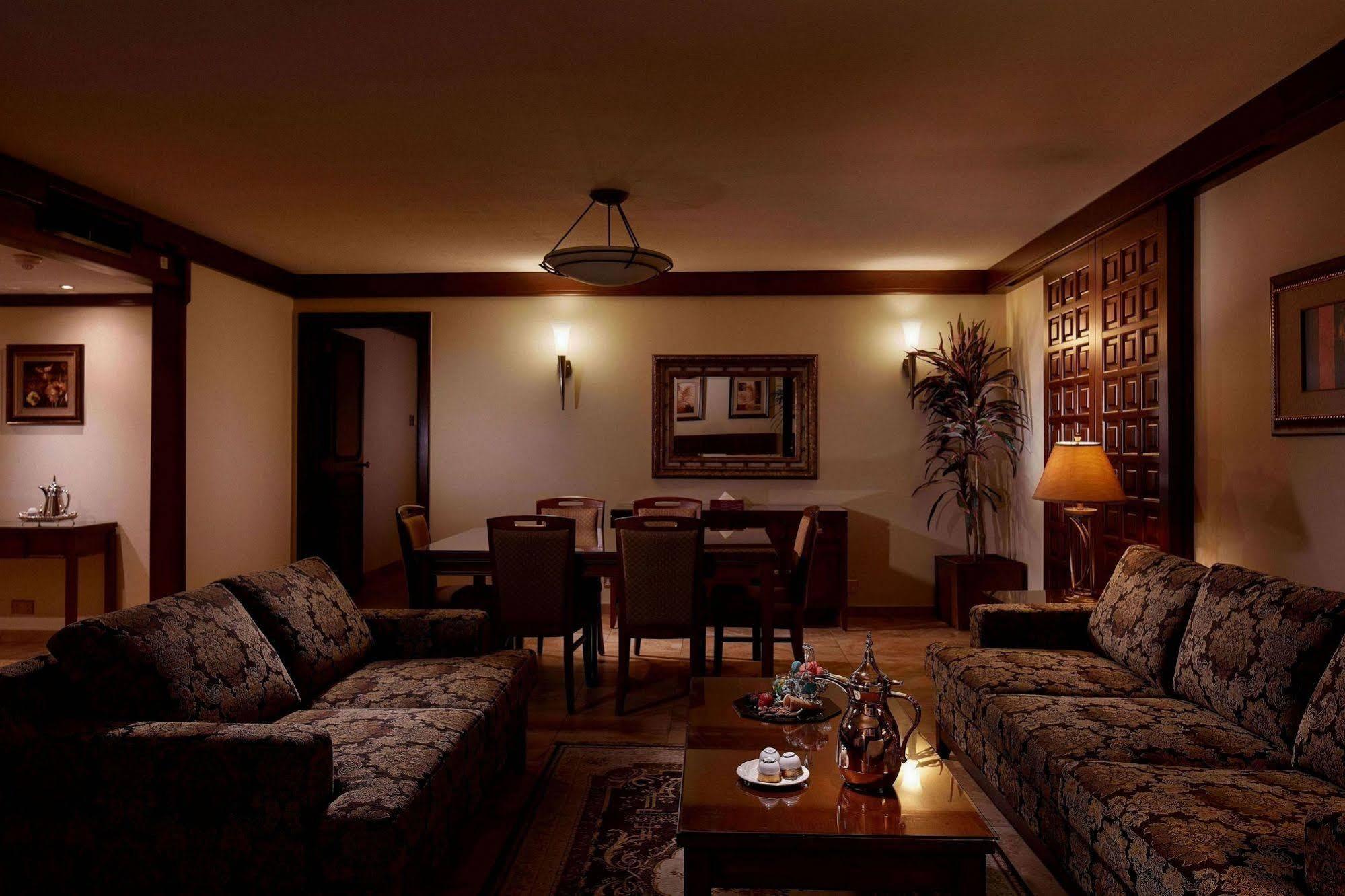 Makarem Ajyad Makkah Hotel Μέκκα Εξωτερικό φωτογραφία The photo depicts a cozy living room setting. It features two patterned sofas facing each other with a wooden coffee table in the center. The room is softly illuminated, creating a warm atmosphere. On the walls, there are decorative elements, includi