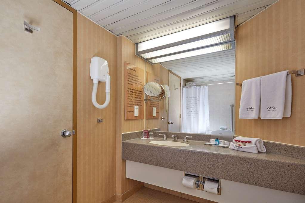 Makarem Ajyad Makkah Hotel Μέκκα Εξωτερικό φωτογραφία The photo shows the interior of a bathroom. It features a light-colored wall with vertical stripes and a ceiling that is white and textured. There is a gray countertop with a sink and a mirror above it. On one side, there are two white towels hanging