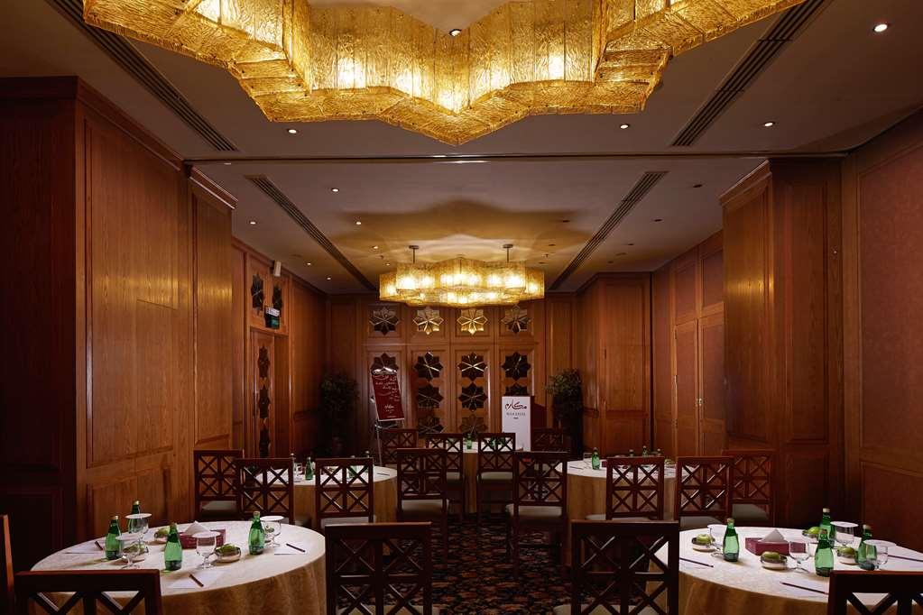 Makarem Ajyad Makkah Hotel Μέκκα Ανέσεις φωτογραφία The photo shows a well-decorated dining room with wooden paneling and elegant furnishings. There are round tables covered with tablecloths, and each table is arranged with glasses of water. The lighting is warm, provided by elaborate chandeliers on t