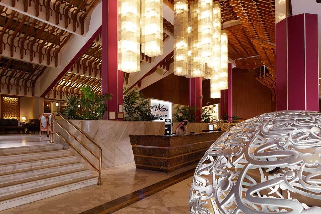 Makarem Ajyad Makkah Hotel Μέκκα Εσωτερικό φωτογραφία The photo depicts a luxurious hotel lobby. It features a grand entrance with a staircase leading up to a reception area. The lobby has high ceilings adorned with striking, modern light fixtures that hang down, providing a warm ambiance. The walls are