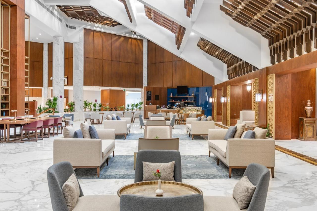 Makarem Ajyad Makkah Hotel Μέκκα Εξωτερικό φωτογραφία The photo depicts the interior of a modern and elegantly designed lobby or lounge area. It features a spacious layout with high ceilings, showcasing a combination of wooden elements and marble flooring. 

In the center, there are several seating arra