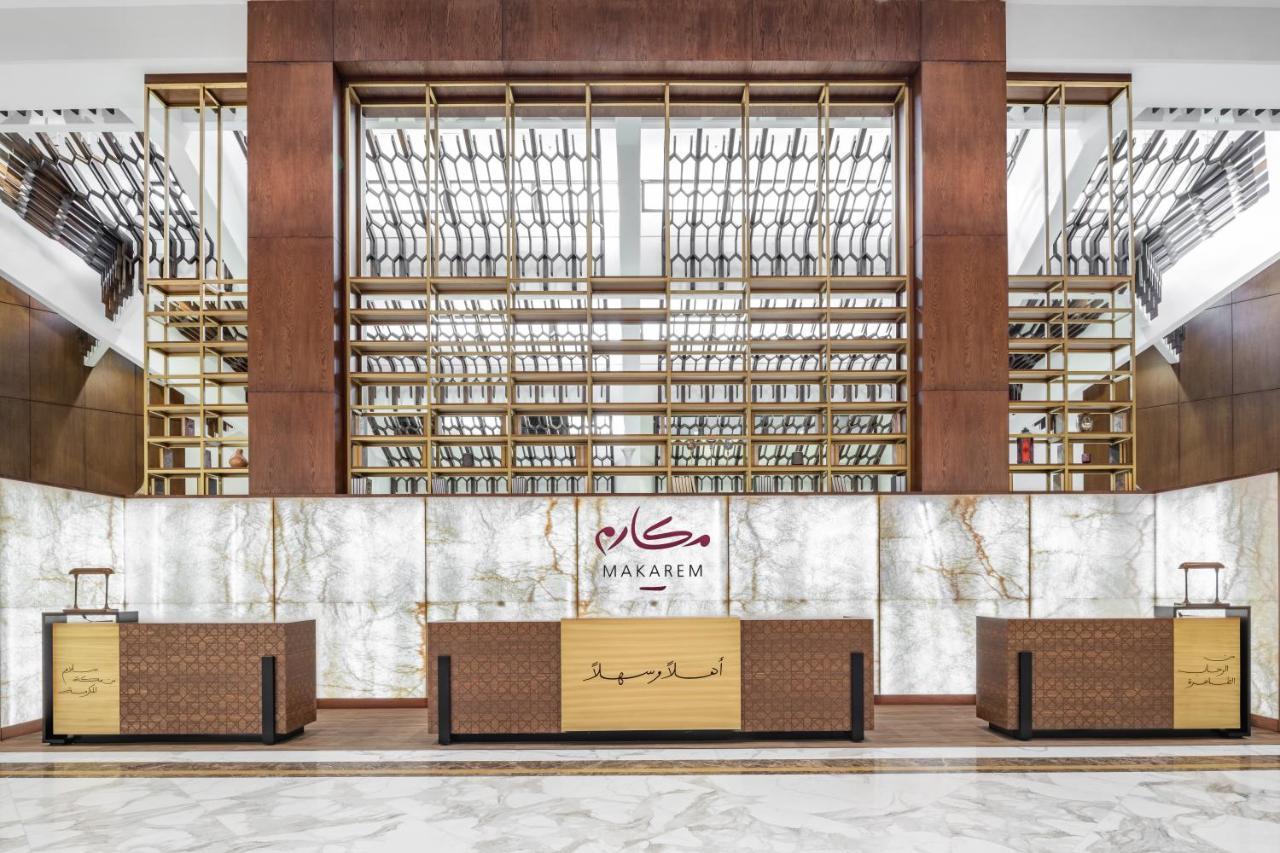 Makarem Ajyad Makkah Hotel Μέκκα Εξωτερικό φωτογραφία The photo shows the interior of a hotel or a reception area, characterized by a modern and elegant design. In the foreground, there are multiple reception desks with a polished finish. Behind the desks, a striking feature is a wooden wall with a geom