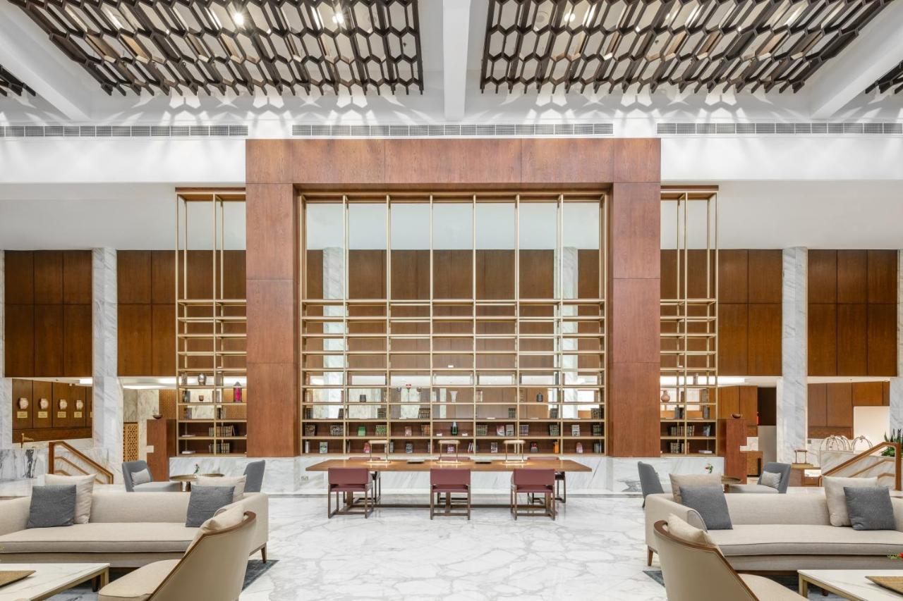 Makarem Ajyad Makkah Hotel Μέκκα Εξωτερικό φωτογραφία The photo shows a spacious interior of a modern lobby or lounge. The design features a large wooden structure with a grid-like pattern in the center, possibly serving as a decorative partition. The walls are adorned with brown wooden panels, and marb