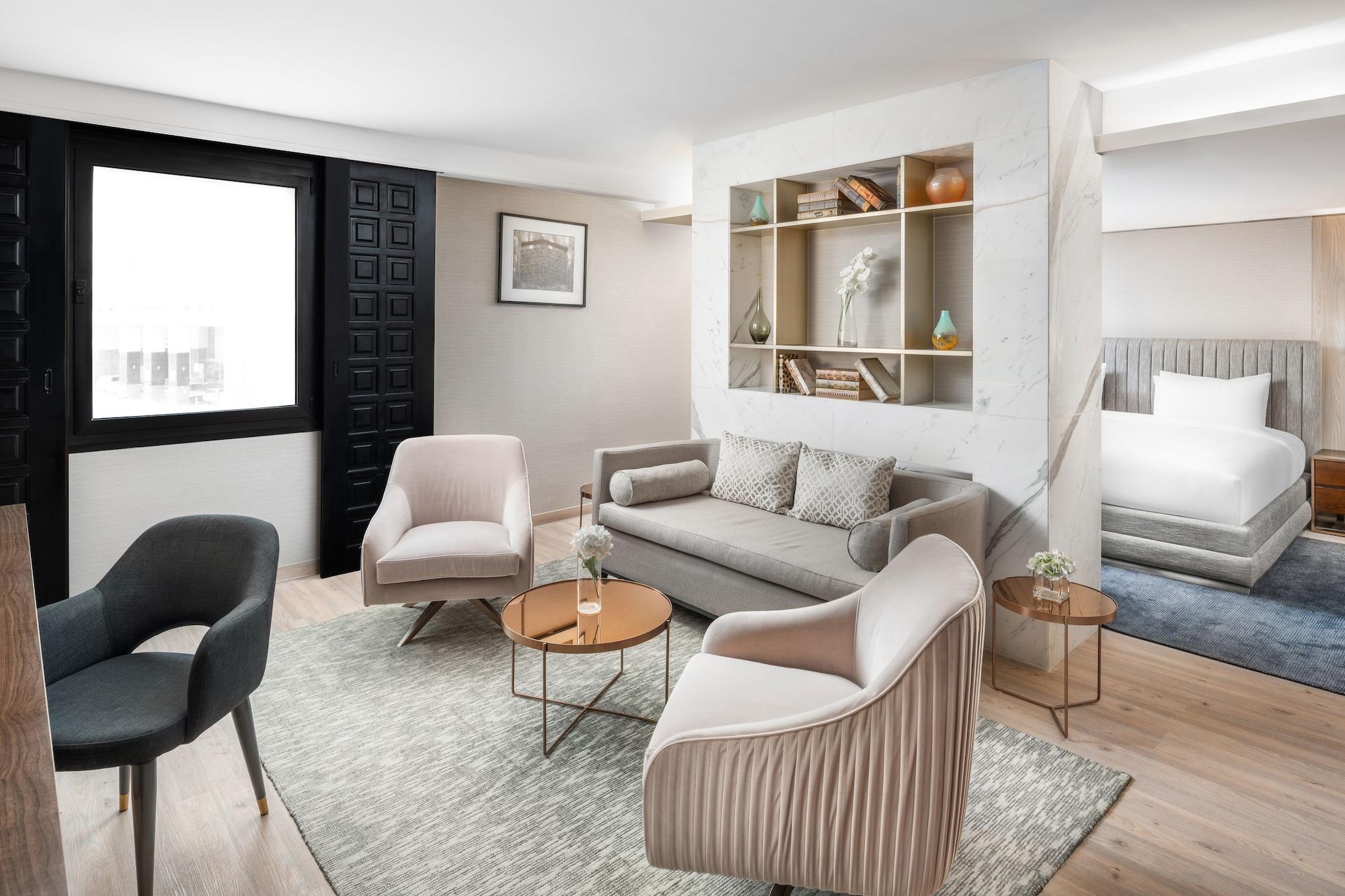 Makarem Ajyad Makkah Hotel Μέκκα Εξωτερικό φωτογραφία The photo shows a stylish and modern living space. There is a comfortable sofa in a neutral color, accompanied by two elegant armchairs and a small round table. The floor is wooden, adding warmth to the room. A decorative shelf in the background feat