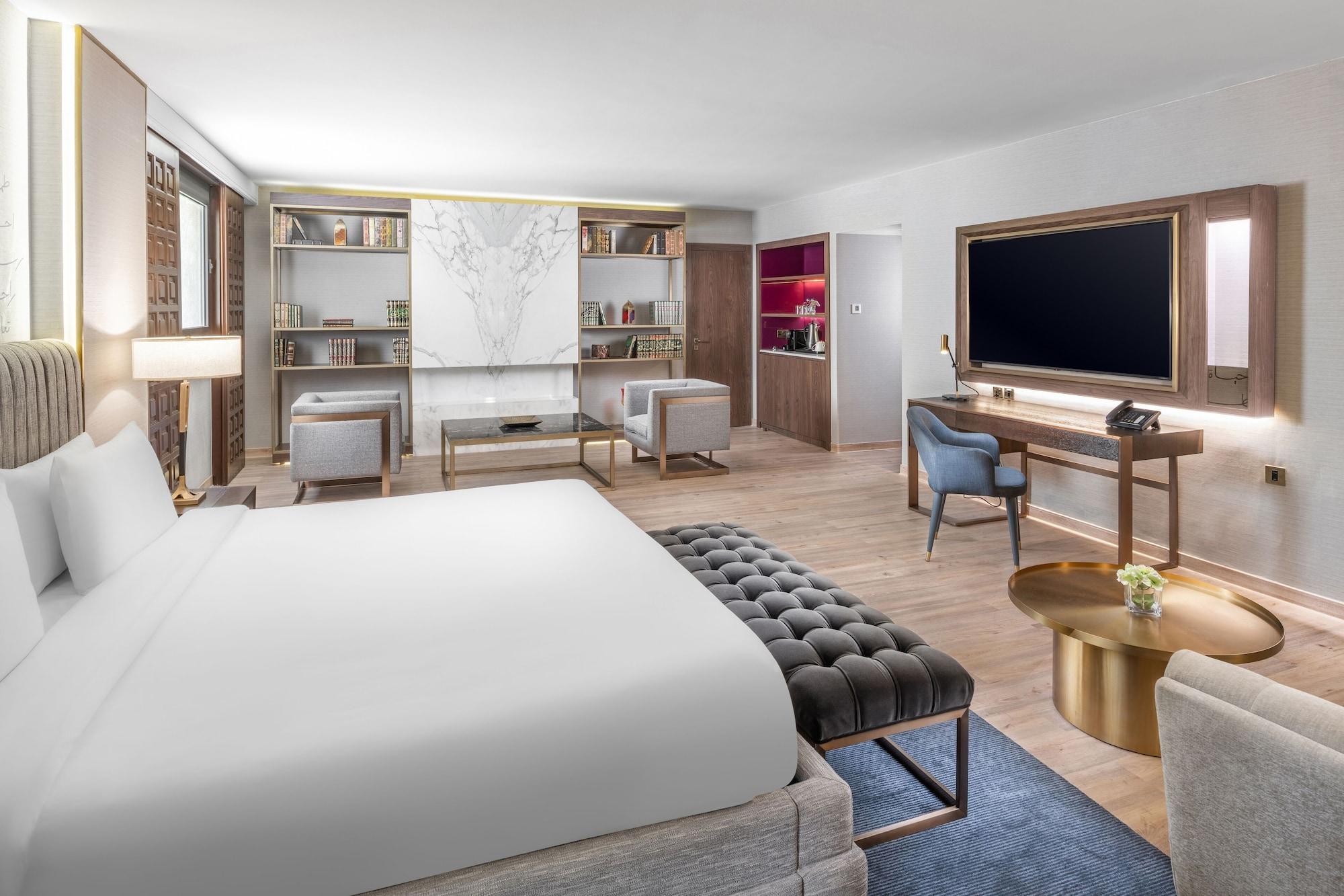 Makarem Ajyad Makkah Hotel Μέκκα Εξωτερικό φωτογραφία The photo shows a modern hotel room designed with a contemporary aesthetic. The room features a large bed with white bedding, complemented by a stylish tufted bench at the foot of the bed. To the side, there are two comfortable armchairs positioned a