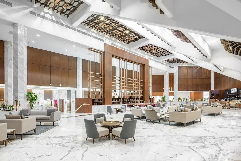 Makarem Ajyad Makkah Hotel Μέκκα Εξωτερικό φωτογραφία The photo shows a spacious and modern hotel lobby. It features a high ceiling with an elegant design, incorporating wooden accents and contemporary lighting. The floor is made of white marble, creating a bright and open atmosphere. 

In the foregroun