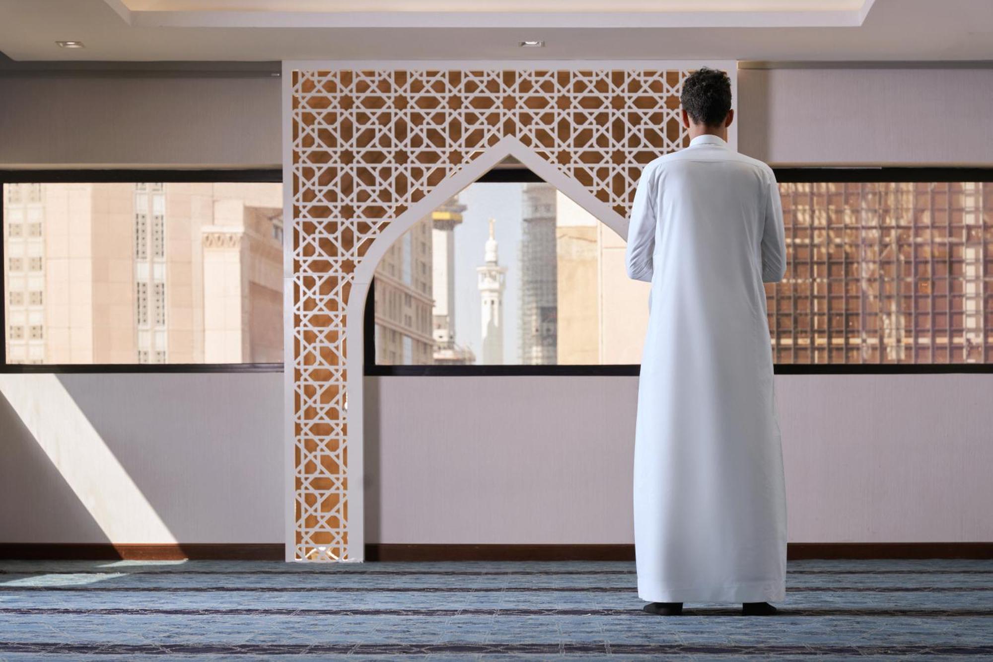Makarem Ajyad Makkah Hotel Μέκκα Εξωτερικό φωτογραφία The photo depicts a person standing with their back facing the viewer, wearing a traditional white garment. They are in a spacious interior setting that features an ornate archway with intricate patterns, typical of Islamic architecture. Through the 