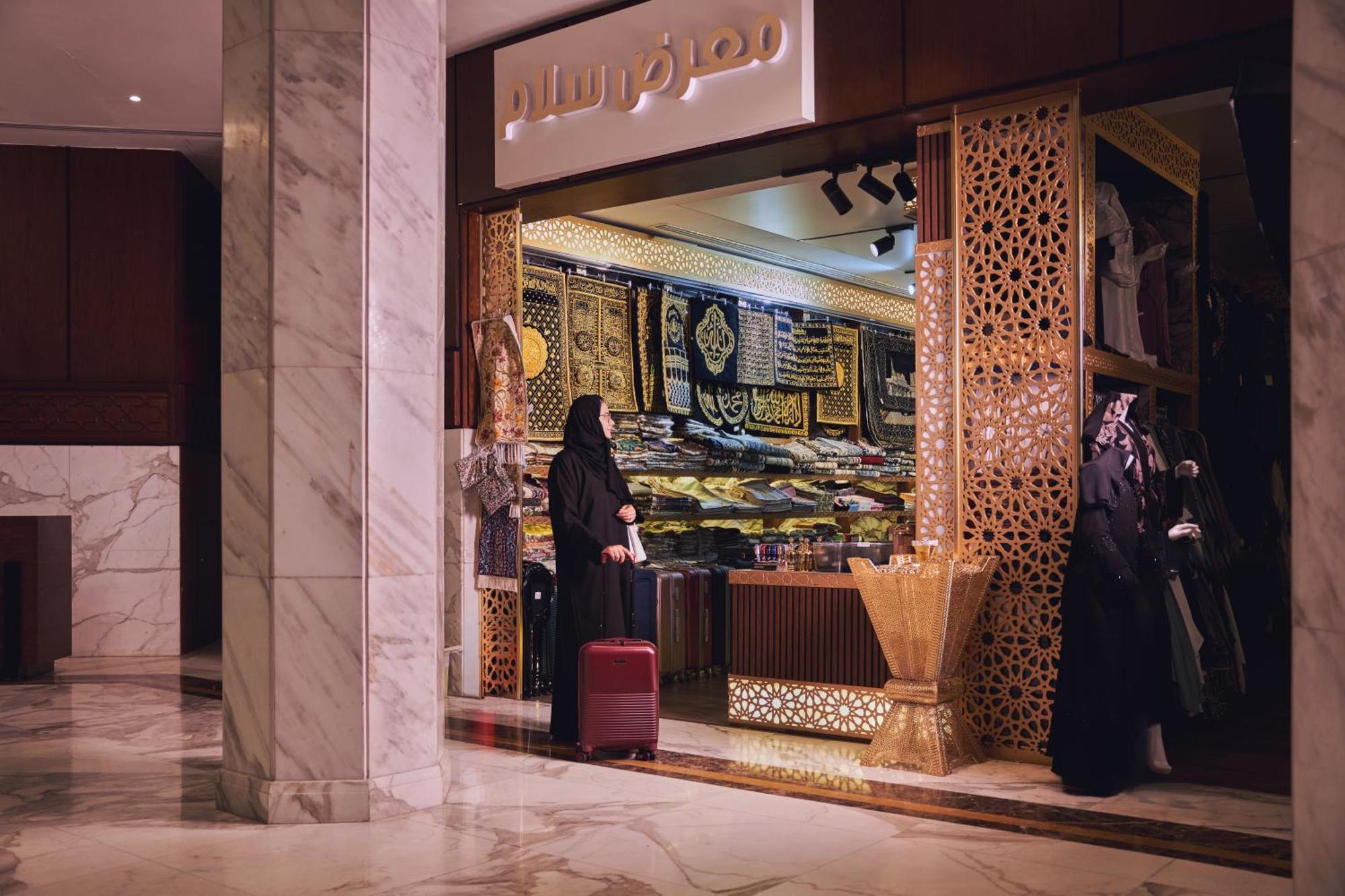 Makarem Ajyad Makkah Hotel Μέκκα Εξωτερικό φωτογραφία The photo shows a storefront that appears to sell traditional textiles or garments. The entrance features intricate decorative patterns, typical of Middle Eastern architecture. A woman is standing outside the shop, dressed in a black abaya, and she h