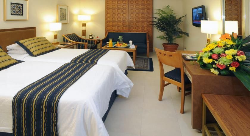 Makarem Ajyad Makkah Hotel Μέκκα Εξωτερικό φωτογραφία The image shows a hotel room featuring two beds with white linens and a decorative stripe along the edge. There is a seating area with two chairs and a small table, set with a breakfast spread that includes fruit and drinks. A small potted plant adds