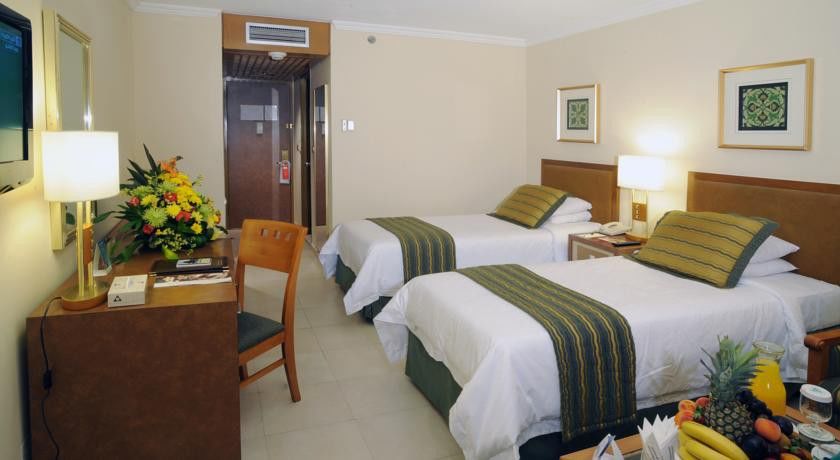 Makarem Ajyad Makkah Hotel Μέκκα Εξωτερικό φωτογραφία The photo shows an interior of a hotel room featuring two twin beds with white linens and green decorative accents. The walls are painted in a light beige color, and there is a small table next to one of the beds. A desk with a chair is positioned ne